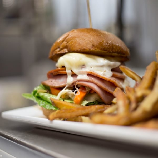 BrewRiver Creole Kitchen's burger with melted cheese, ham, lettuce, and fries on a white plate.