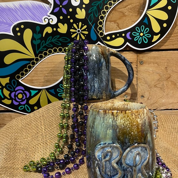 Mardi Gras mask and beads with two BrewRiver Creole Kitchen mugs on burlap.