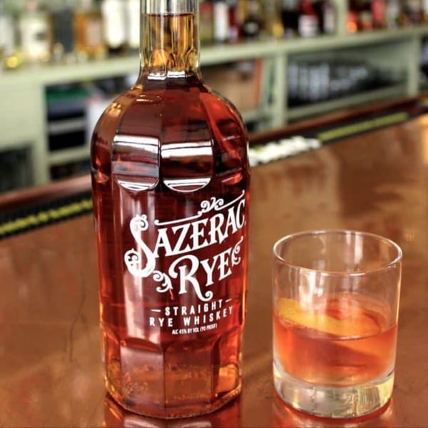 A bottle of Sazerac Rye whiskey next to a glass of whiskey with an orange peel.