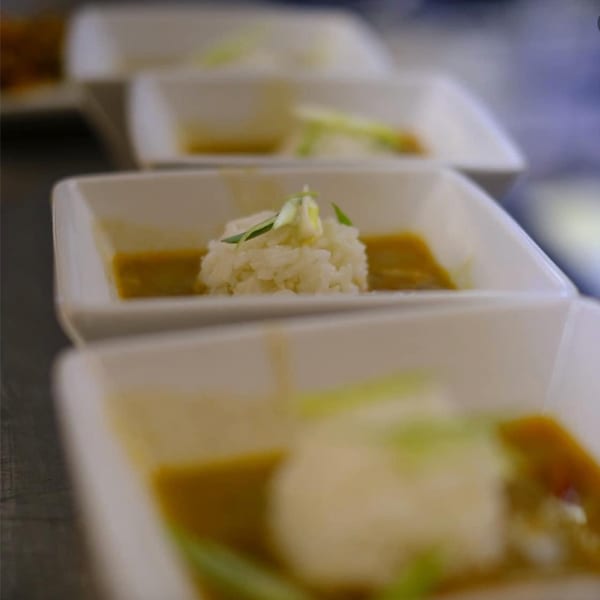 A row of white square bowls with Creole gumbo and a scoop of rice, garnished with green onions.