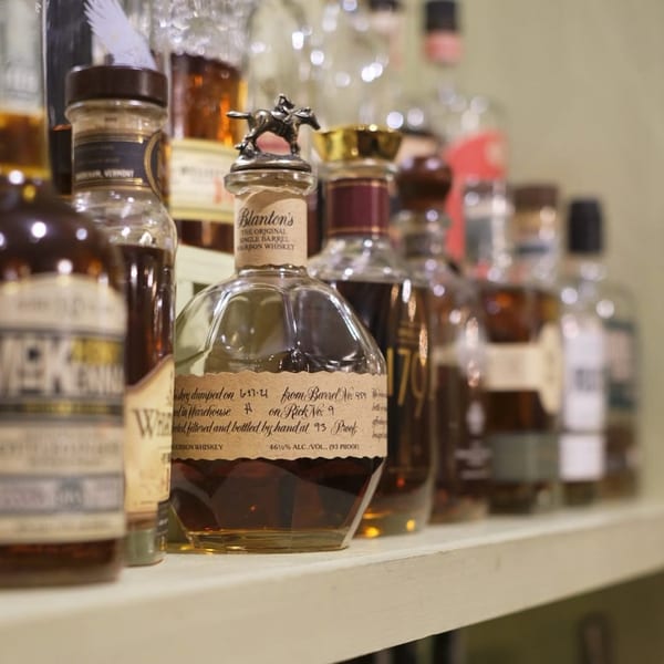A close-up of various whiskey bottles, including Blanton's, on a shelf at BrewRiver Creole Kitchen.