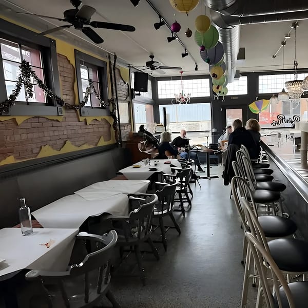 BrewRiver Creole Kitchen's dining room with exposed brick, ceiling fans, and patrons at tables and bar.