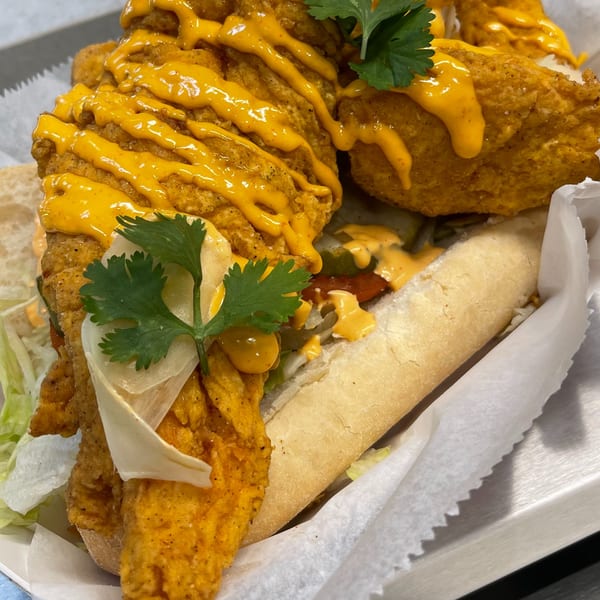 A close-up of a BrewRiver Creole Kitchen fried fish po'boy sandwich with sauce and cilantro.