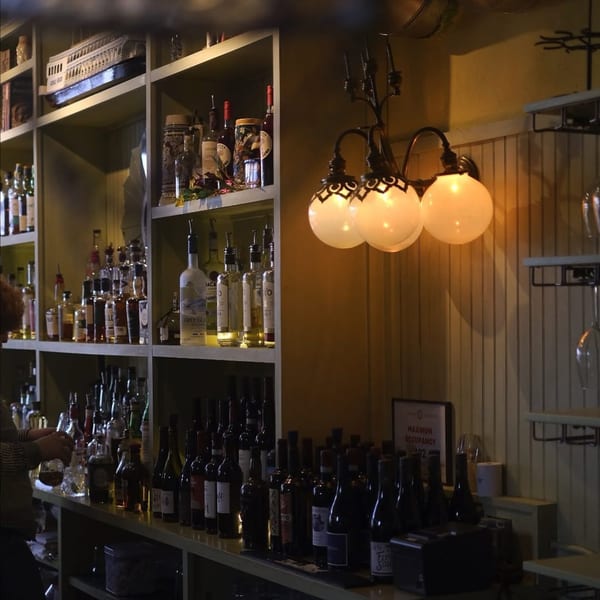 A bartender mixes a drink at BrewRiver Creole Kitchen's bar, with liquor bottles and a decorative boat.